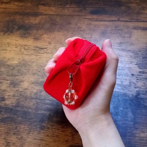丸縁のお守りを付けたミニタロットカード入れの赤いポーチ